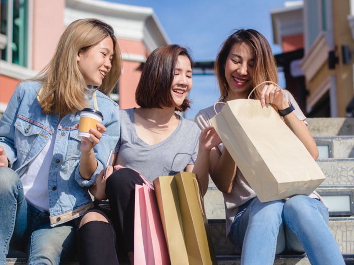 Three friends with shopping bags sitting on outdoor steps